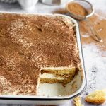 Front angle view of pandoro tiramisu with cocoa powder in the background