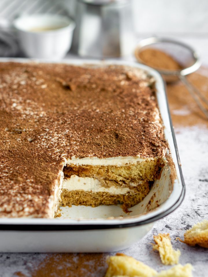 Pandoro tiramisu in a white pan with cocoa powder in the background