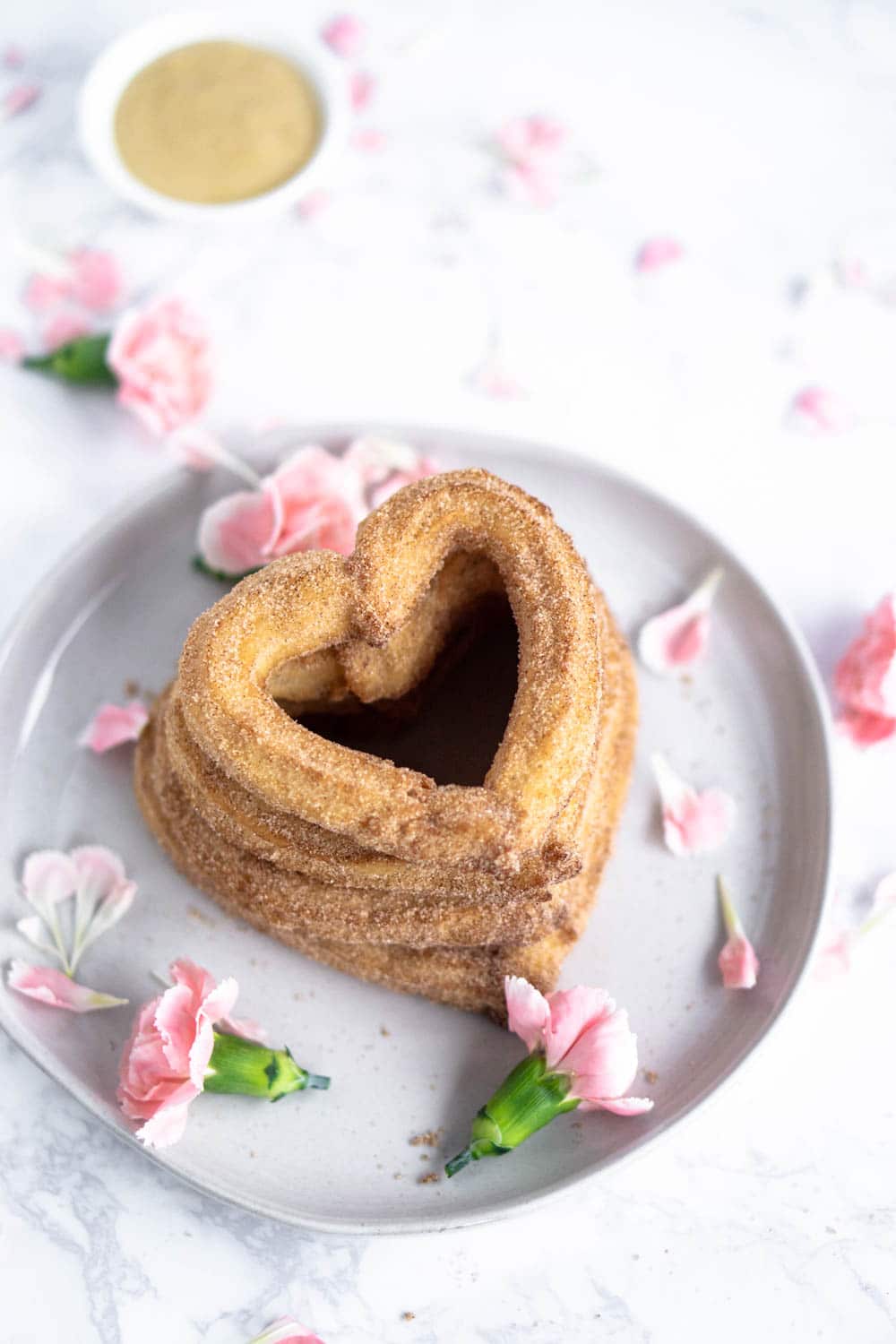 Heart shaped churros for Valentine's Day with mascarpone and nutella dipping sauces #valentinesday #valentinesdaybaking #valentinesdaydesserts #churros #heartchurros heart shaped churros stacked on a plate with pink flowers
