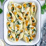 Stuffed Pasta Shells in a white pan surrounded by spinach and fresh ricotta