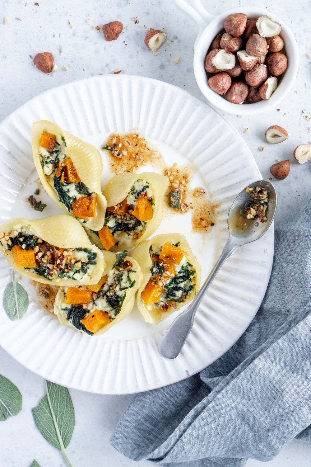 Vegetarian stuffed pasta shells with butternut squash, ricotta and spinach. They're baked to perfection and topped with a brown butter, sage and hazelnut sauce! #stuffedshells #pastashells #pinacooks Stuffed pasta shells on a white plate