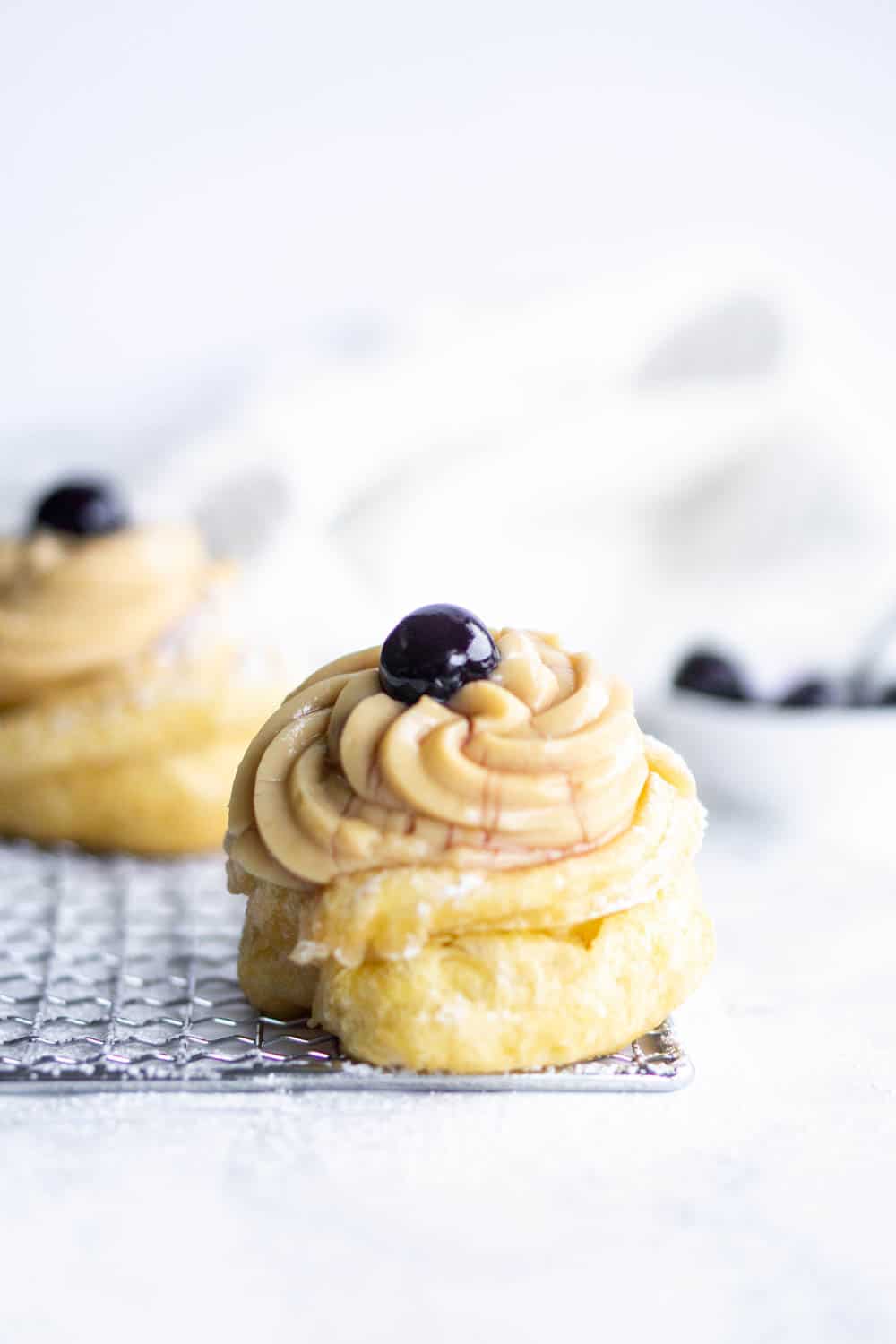 These fritters are made in Italy on the feast of Saint Joseph. They're called zeppole di San Giuseppe in Italian #pinacooks #italiandesserts #zeppoledisangiuseppe straight-on shot of zeppole di san Giuseppe with amarene and a napkin in the background