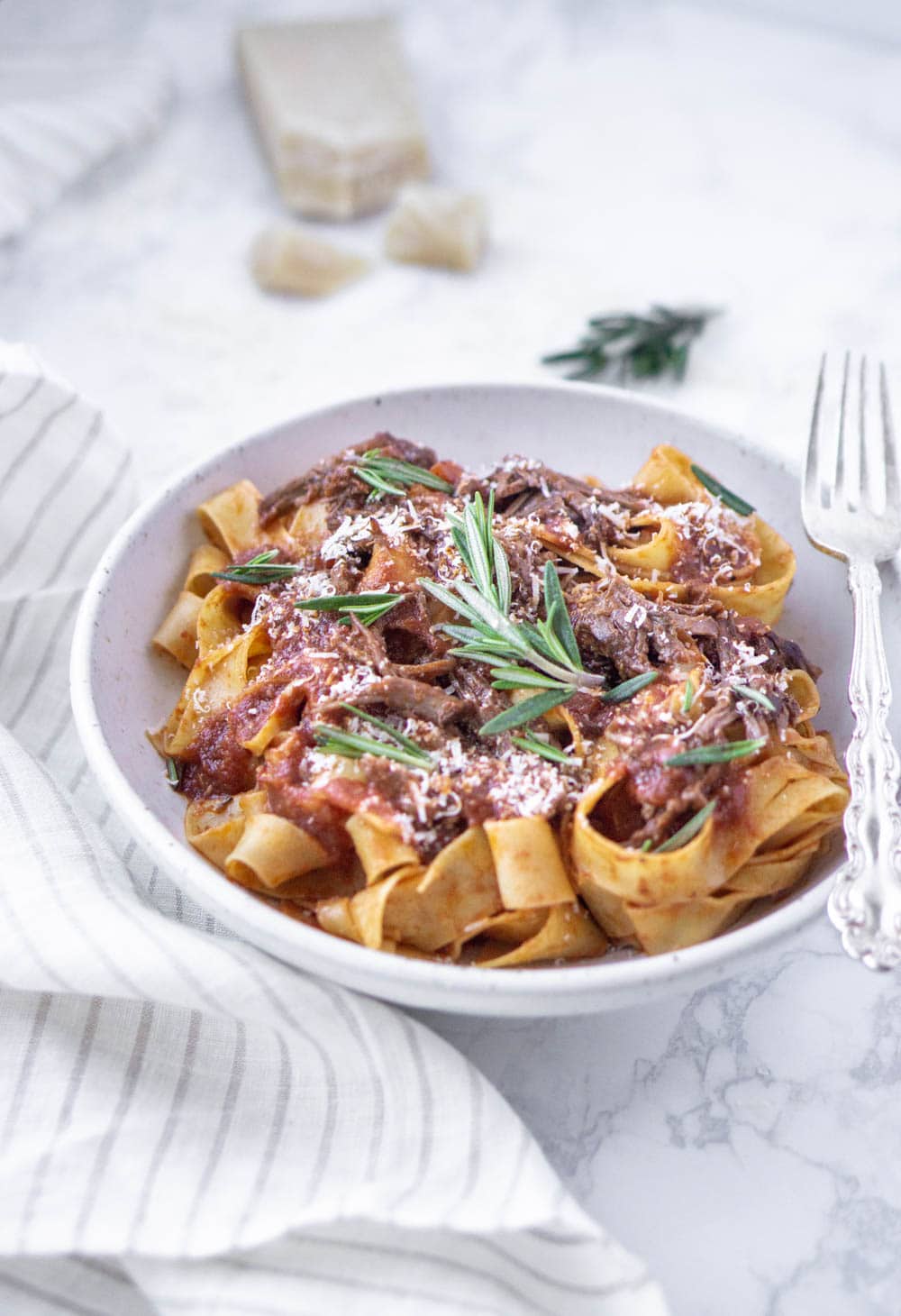 Short Rib Ragu! The best Sunday Sauce ever! #italianfood #italianrecipes #shortribragu #pinacooks beef short rib pappardelle in a white plate with parmesan and rosemary in the background