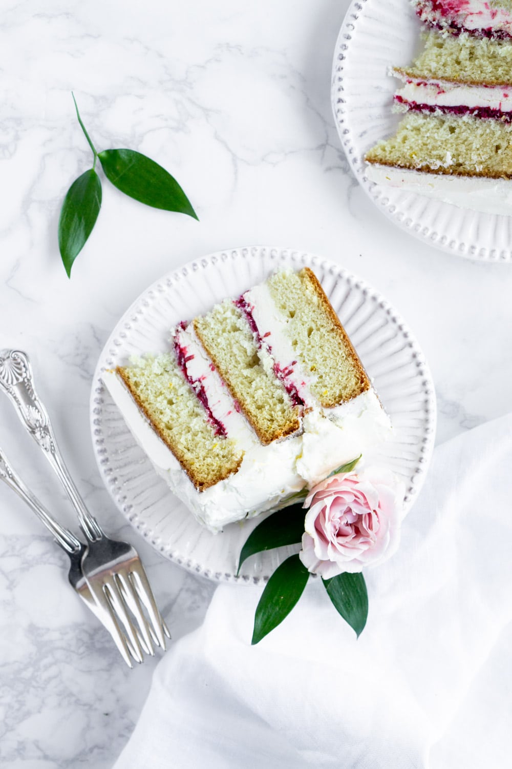 Beauty of a cake! Raspberry limoncello cake with limoncello buttercream. Yum! #layercake #limoncellocake #pinacooks a slice of limoncello cake on a plate with two forks