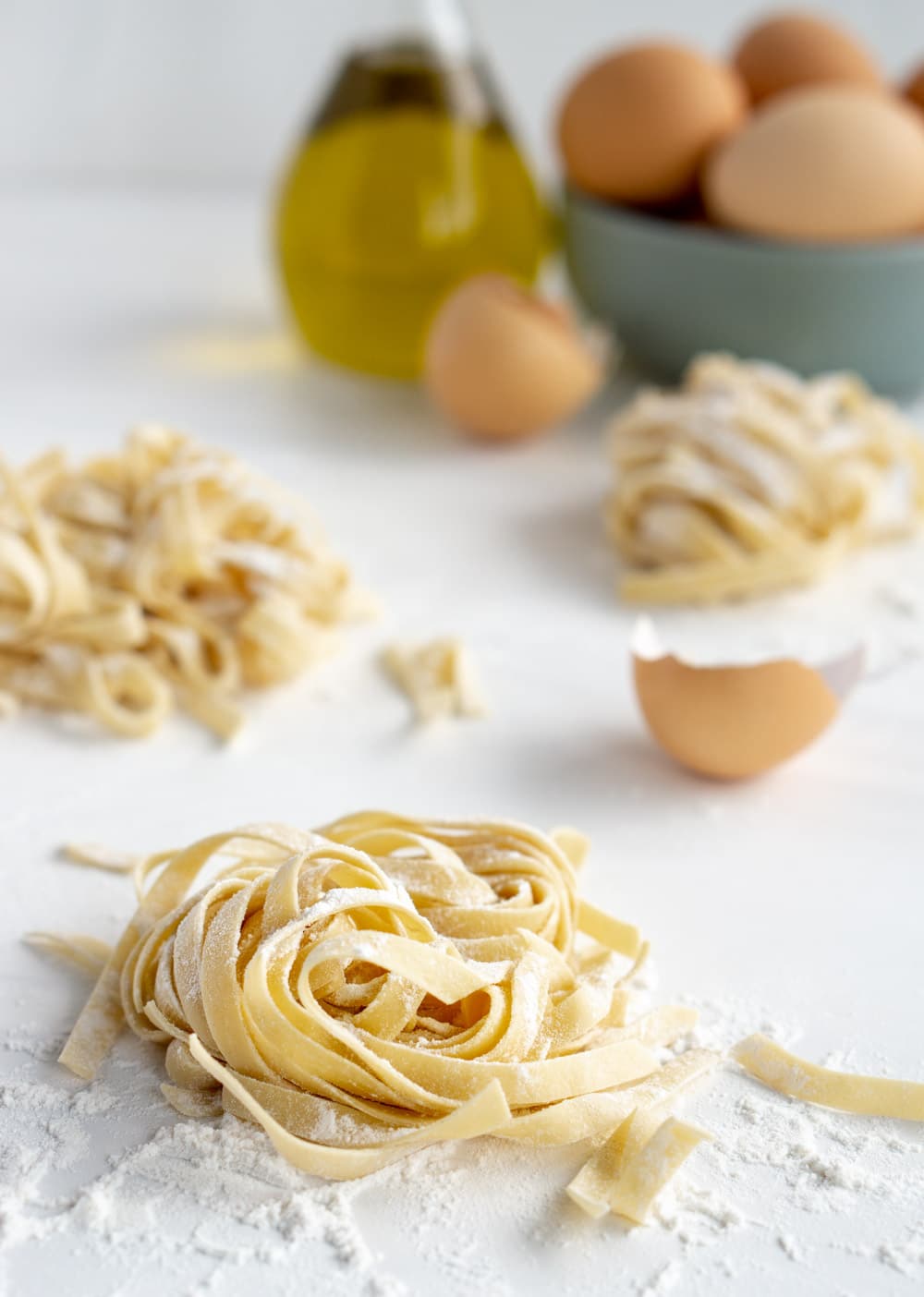 The KitchenAid pasta attachment makes making homemade pasta so easy! Just follow this simple process. #pinacooks #homemadepasta #freshpasta Fresh pasta nest with eggs and olive oil in the background
