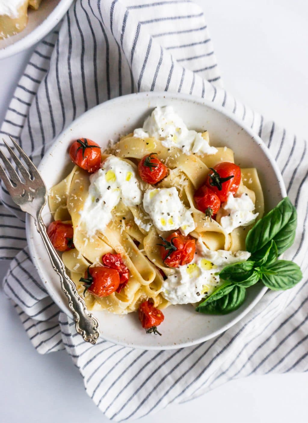 Bowl of pappardelle pasta with cherry tomato and burrata sauce with a striped napkin