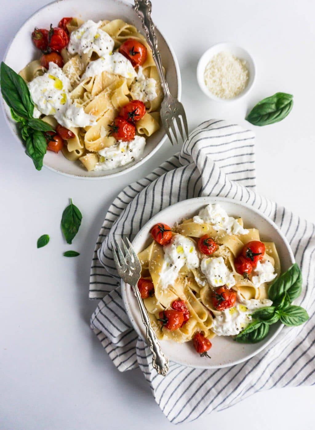 Two bowls of cherry tomato pasta with burrata, and a small bowl of parmesan to the side