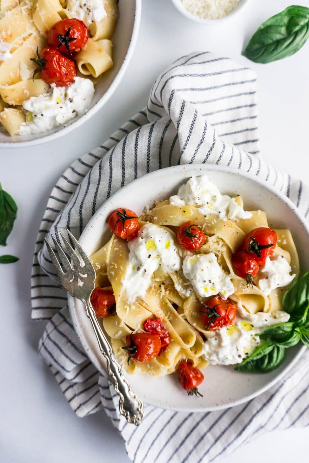 Burst cherry tomato pasta with burrata in a plate garnished with fresh basil