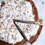Overhead shot of nutella tart topped with whipped cream with one slice cut from the tart