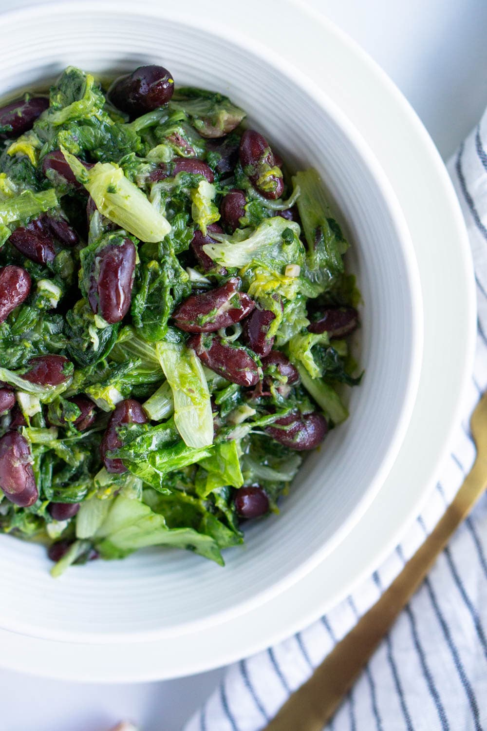Escarole and beans. A comforting Italian side dish! #pinacooks #italianfood #escarole #sidedish Plate of escarole and dark beans with a striped napkin