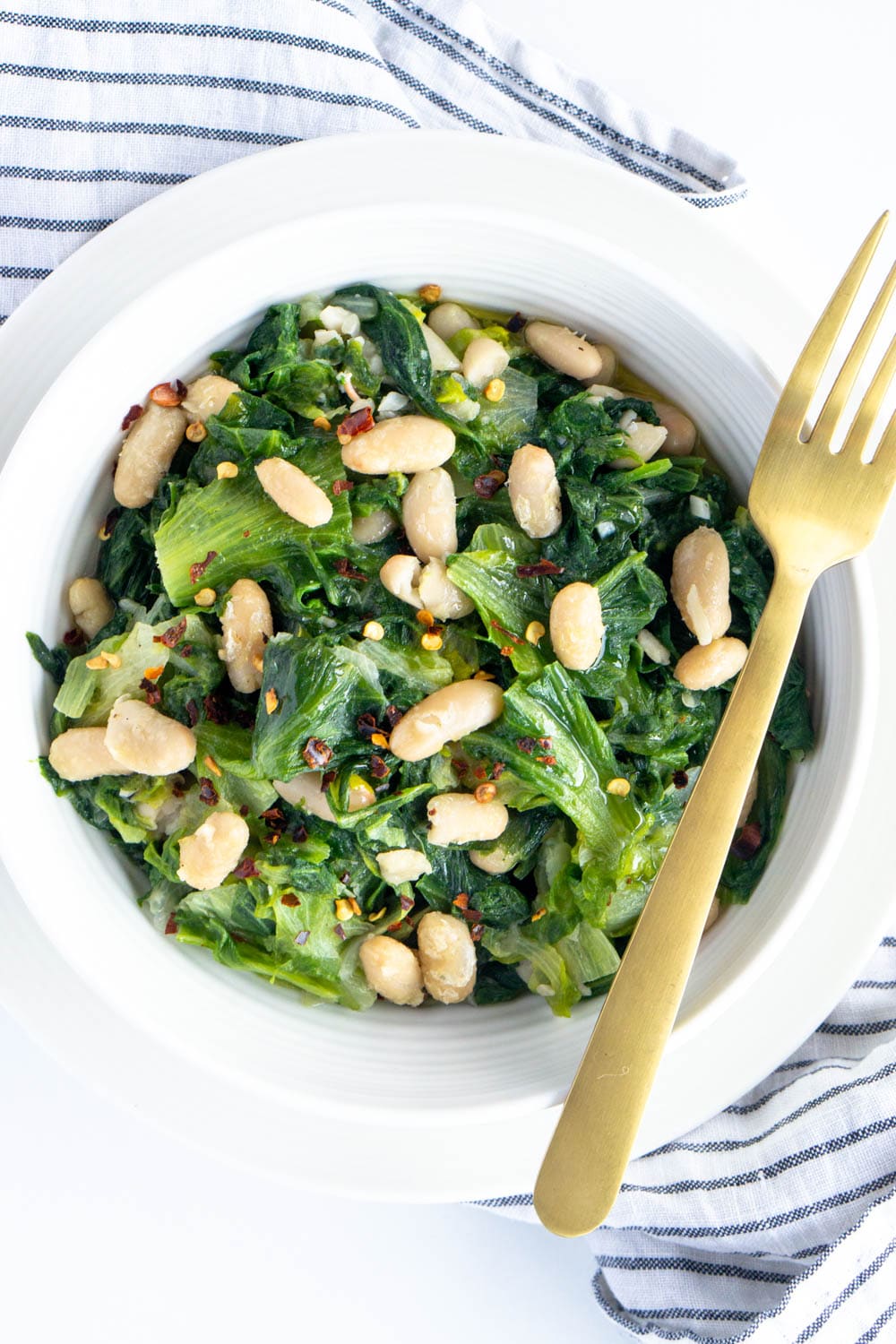 Escarole and beans. A comforting Italian side dish! $pinacooks #escarole #escaroleandbeans Overhead shot of escarole and beans with a napkin and gold fork