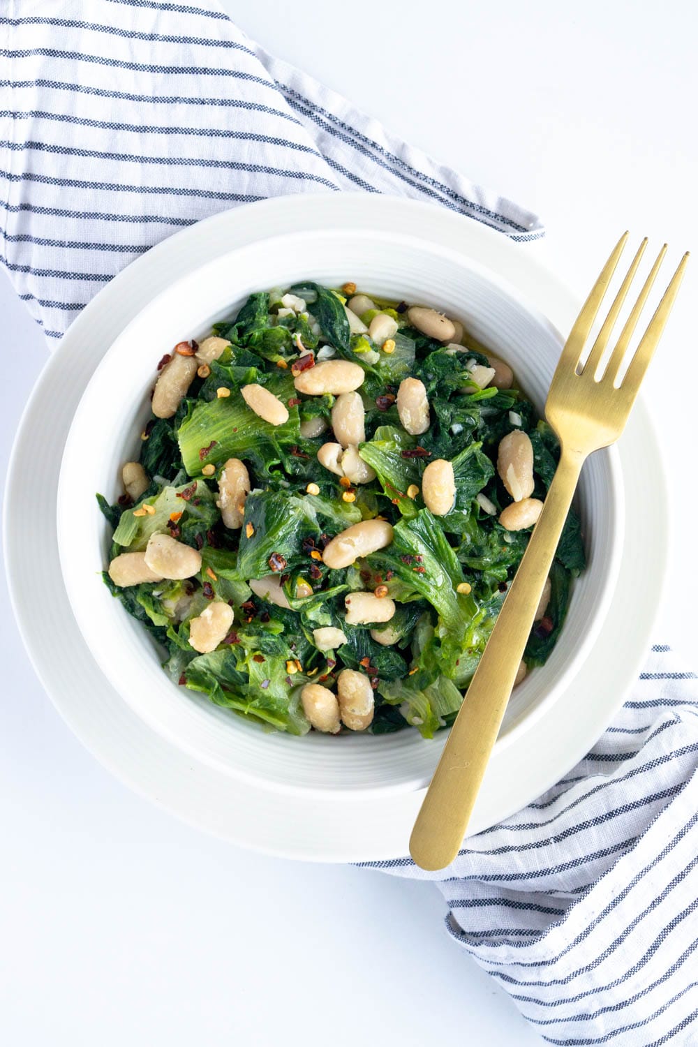 Escarole and beans. A comforting Italian side dish! #pinacooks #italianfood #escarole #sidedish Plate of escarole and beans centered on the image with a napkin underneath