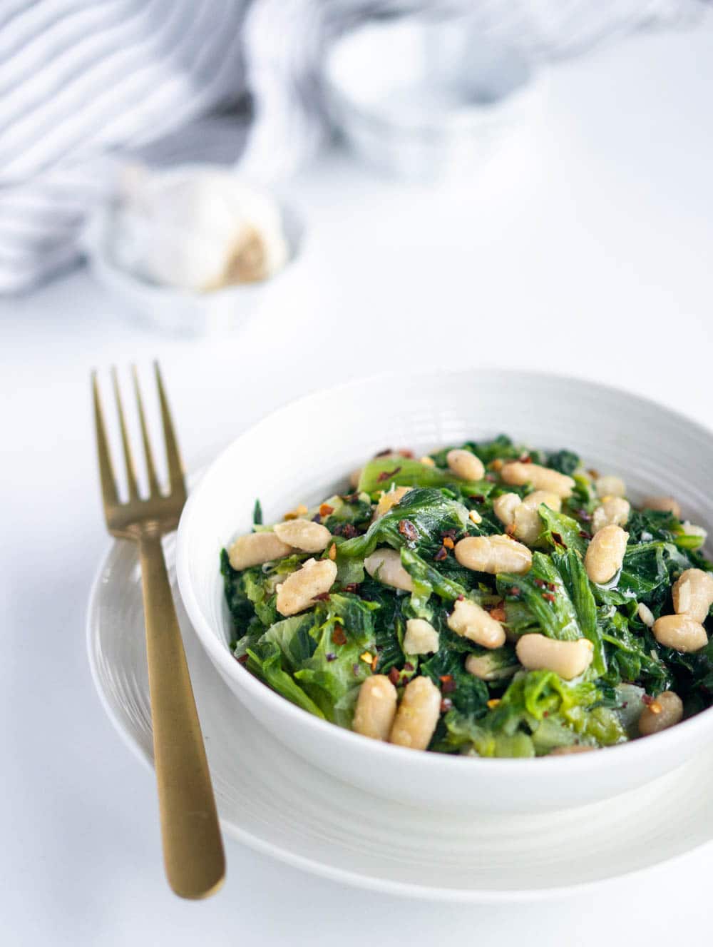 Escarole and beans. A comforting Italian side dish! #pinacooks #italianfood #escarole #sidedish Side view of a dish of escarole and beans with garlic in the background