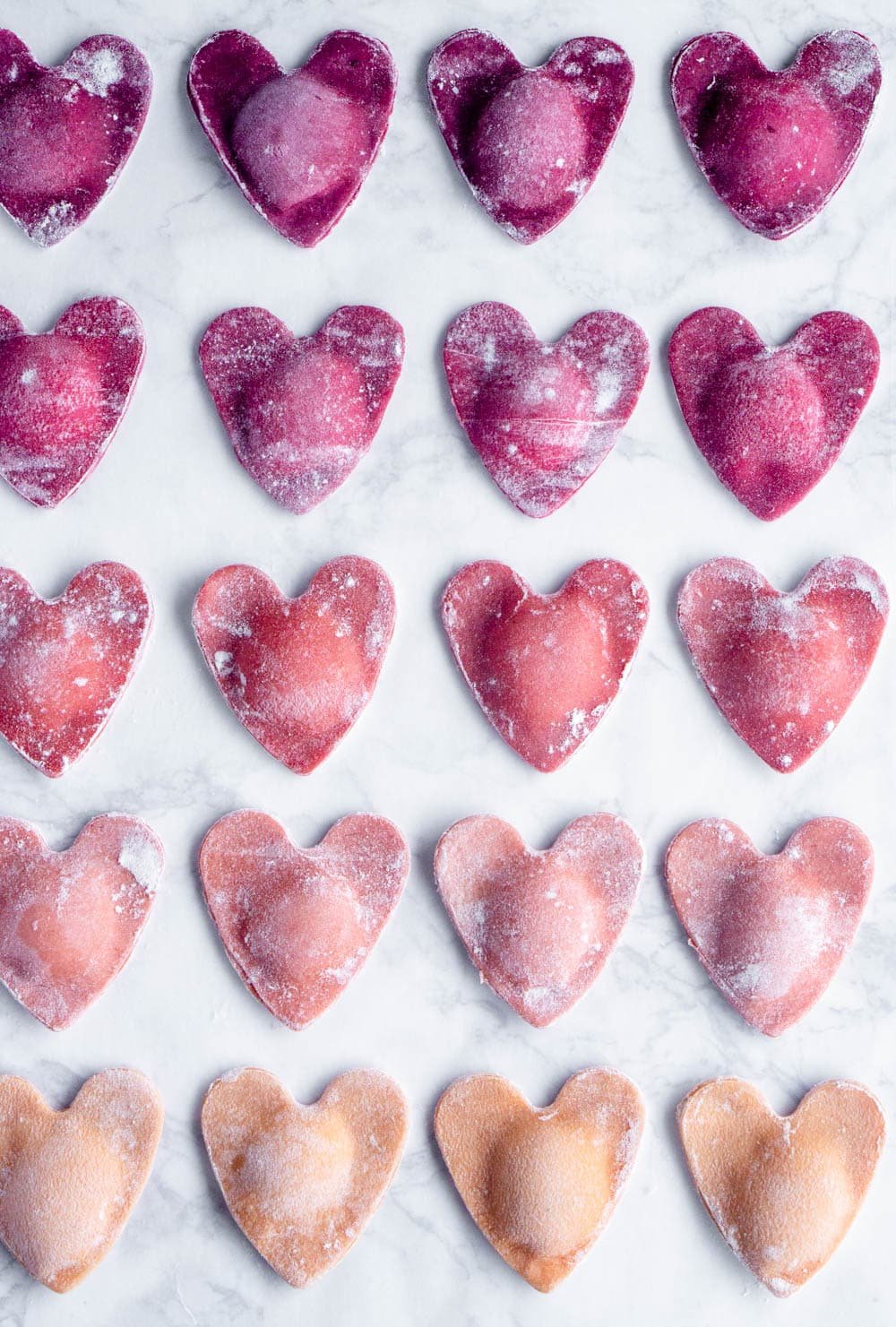Overhead shot of ombré beet ravioli hearts on a marble background