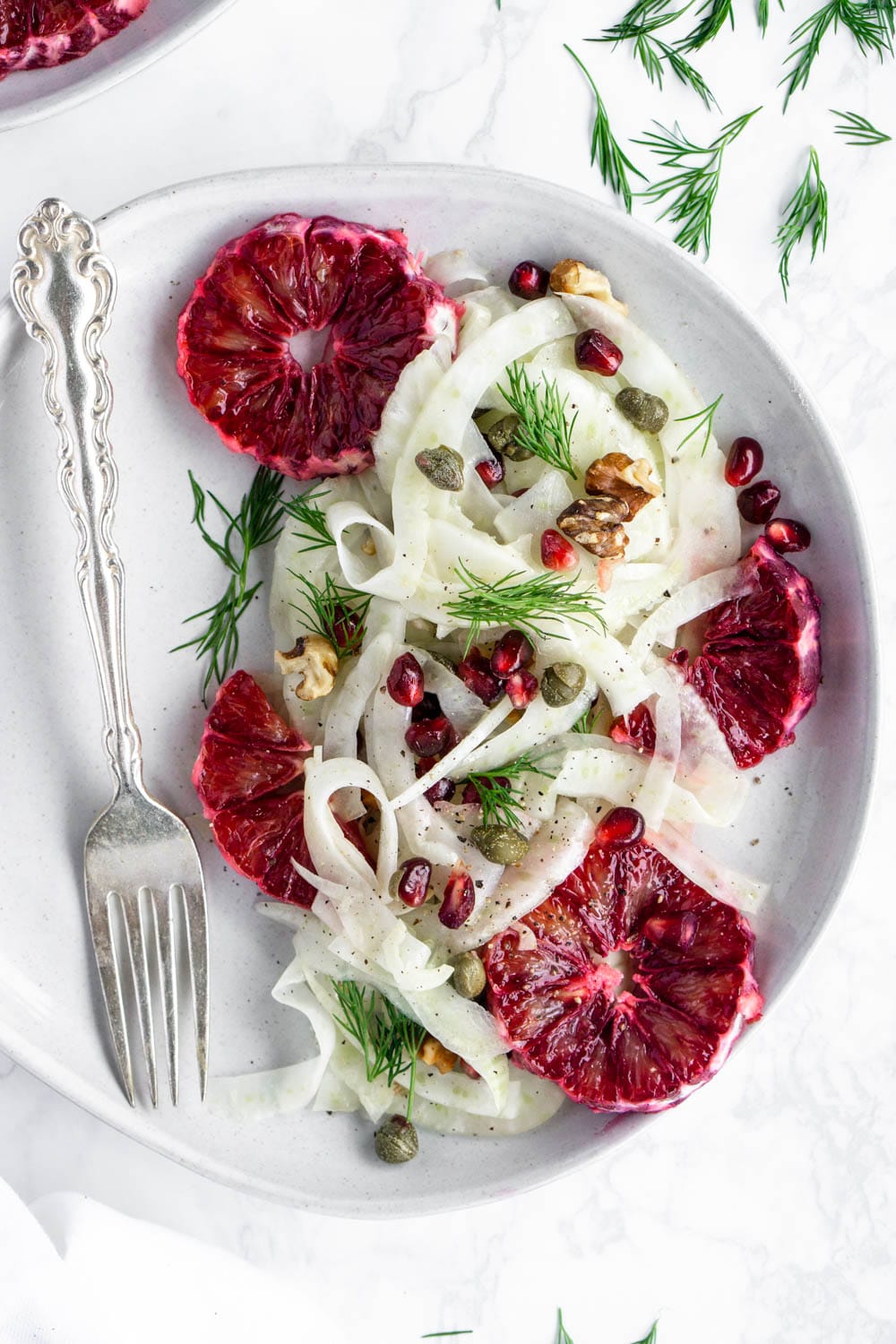 Such a stunning salad! Shaved fennel with blood orange, pomegranate, capers, walnuts, and a white balsamic dressing. #fennelsalad #bloodorangesalad #wintersalad #fennelrecipe #pinacooks Overhead shot of a fennel salad with blood oranges in a plate