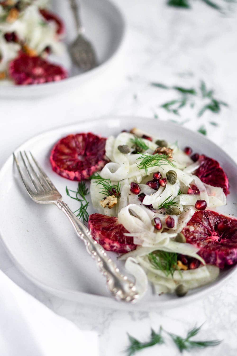 This easy salad is made with shaved fennel, blood oranges, pomegranate and walnuts with white balsamic dressing #fennelsalad #bloodorangesalad #wintersalad #fennelrecipe #pinacooks Side shot of a fennel salad with blood oranges and a sprinle of fresh dill in the background