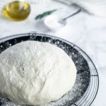 pizza dough on a black plate with olive oil and rosemary in the background