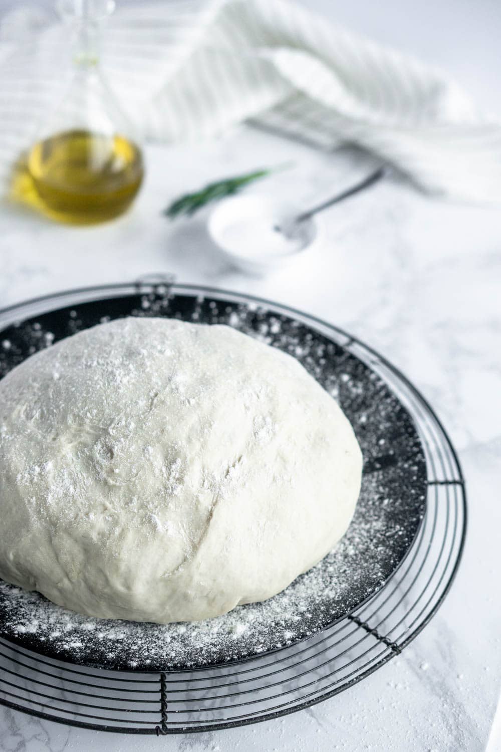 How to make no-knead pizza dough! just let the KitchenAid mixer do all the work for you. #pizzadough #nokneadpizzadough #pinacooks pizza dough on a black plate with olive oil and rosemary in the background