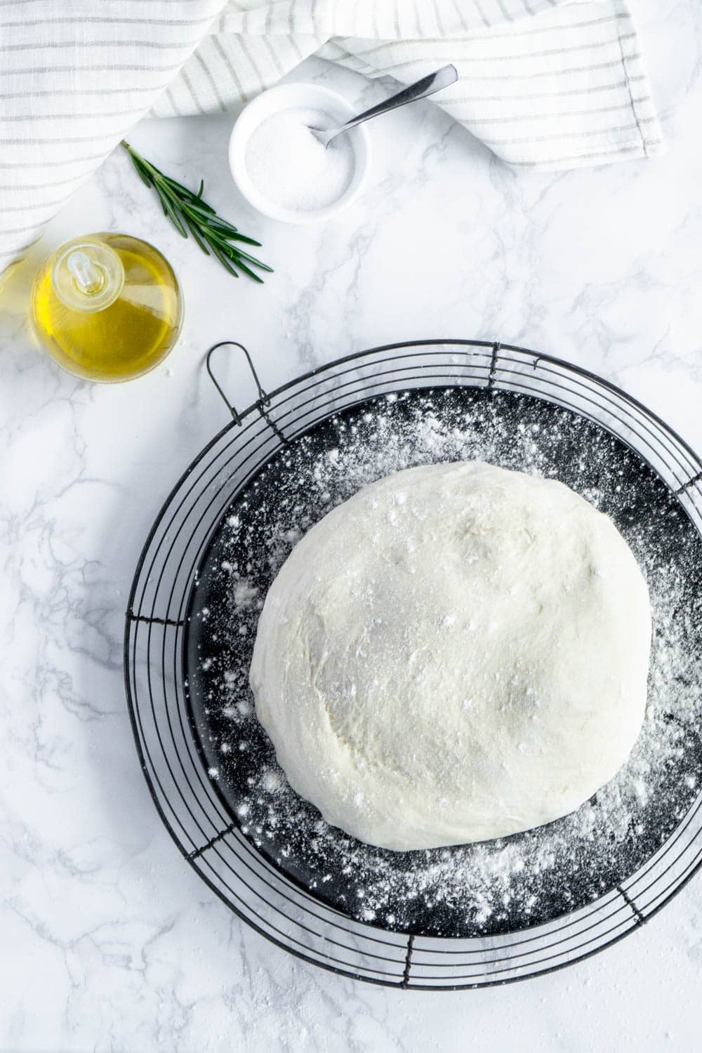 Homemade pizza dough. And it's no knead! #pinacooks #pizzadough #nokneadpizzadough Overhead shot of pizza dough on a black plate with flower sprinkled on top