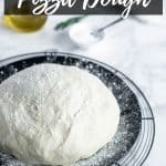 side shot of pizza dough on black plate with flour sprinkled on top