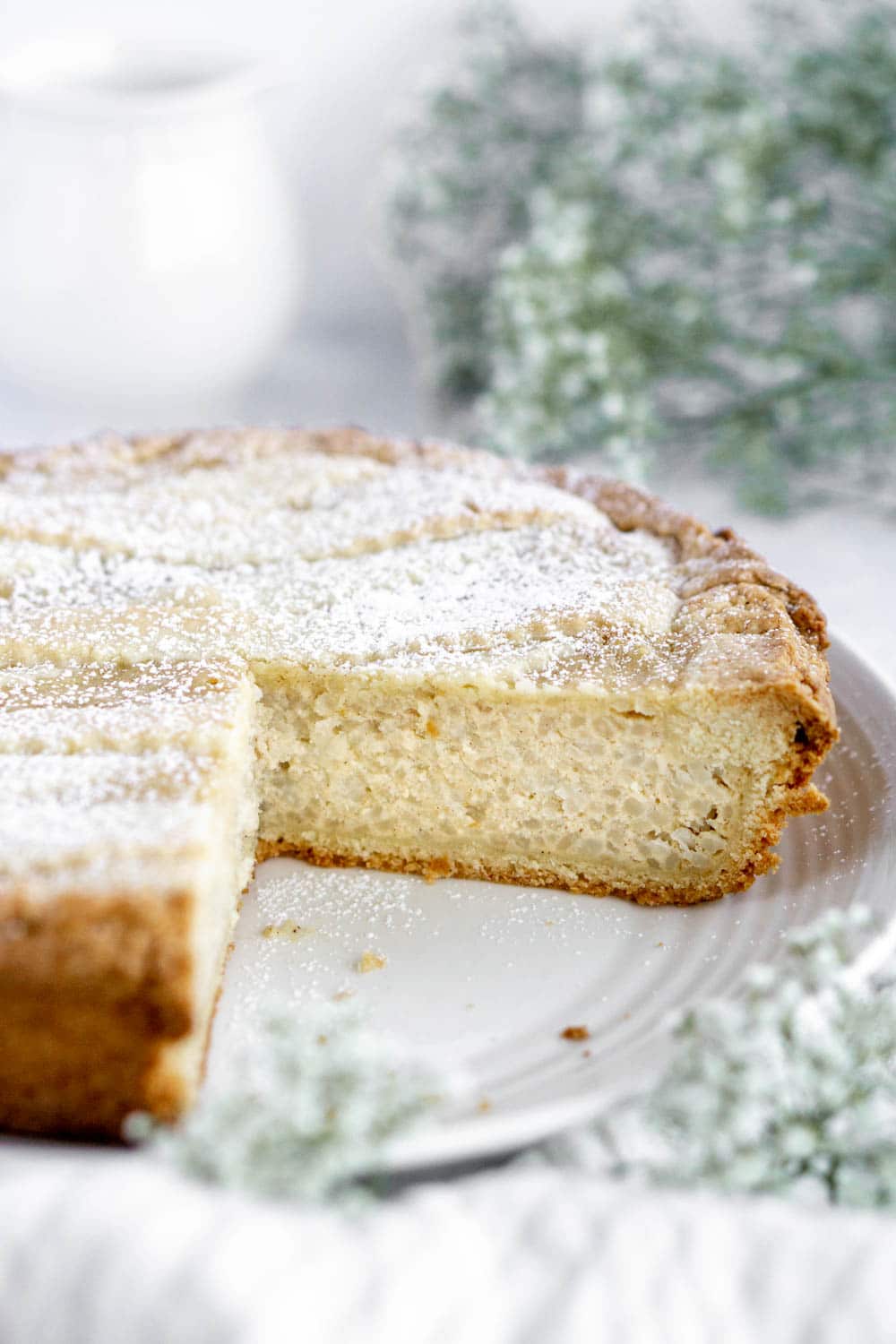 Italian rice pie on a plate with a slice cut out and flowers in the background