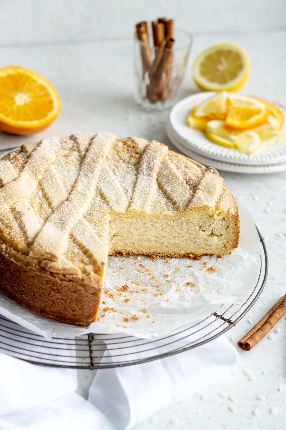A sweet Easter rice pie sitting on a cooling rack with oranges and cinnamon sticks in the background