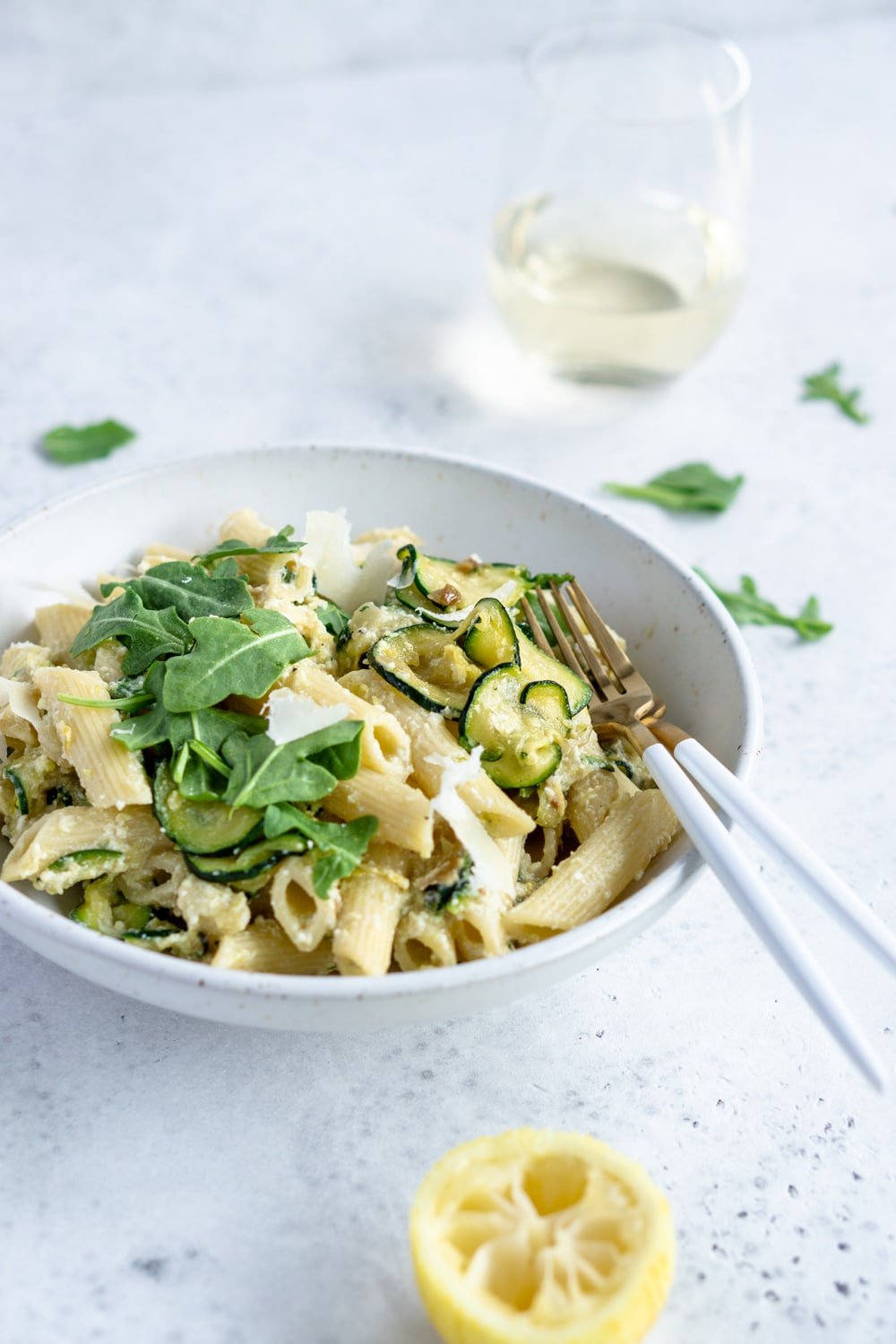 Creamy ricotta pasta with zucchini and arugula. An easy and delicious dish! #italianfood #pinacooks #ricottapasta ricotta pasta in a plate with two forks in the plate and a glass of white wine in the background