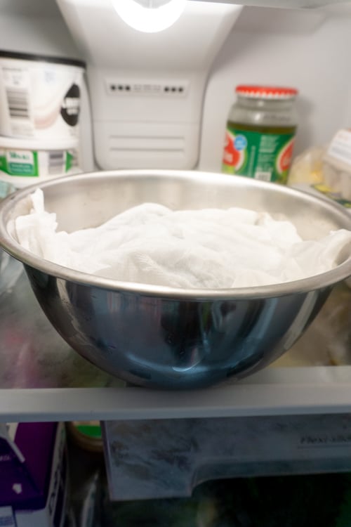 Bowl of mussels in fridge covered with a damp paper towel