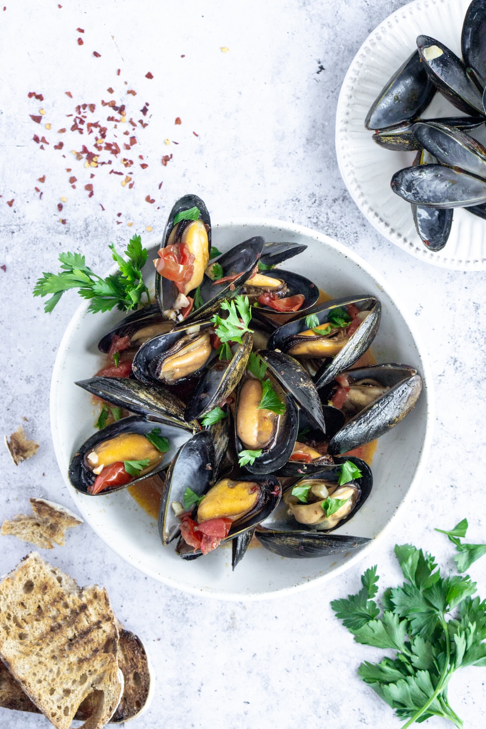 Steamed Mussels recipe with white wine, garlic and tomato broth. #mussels #steamedmussels #pinacooks #italianfood Top view of plate of cooked mussels in a white wine and tomato sauce