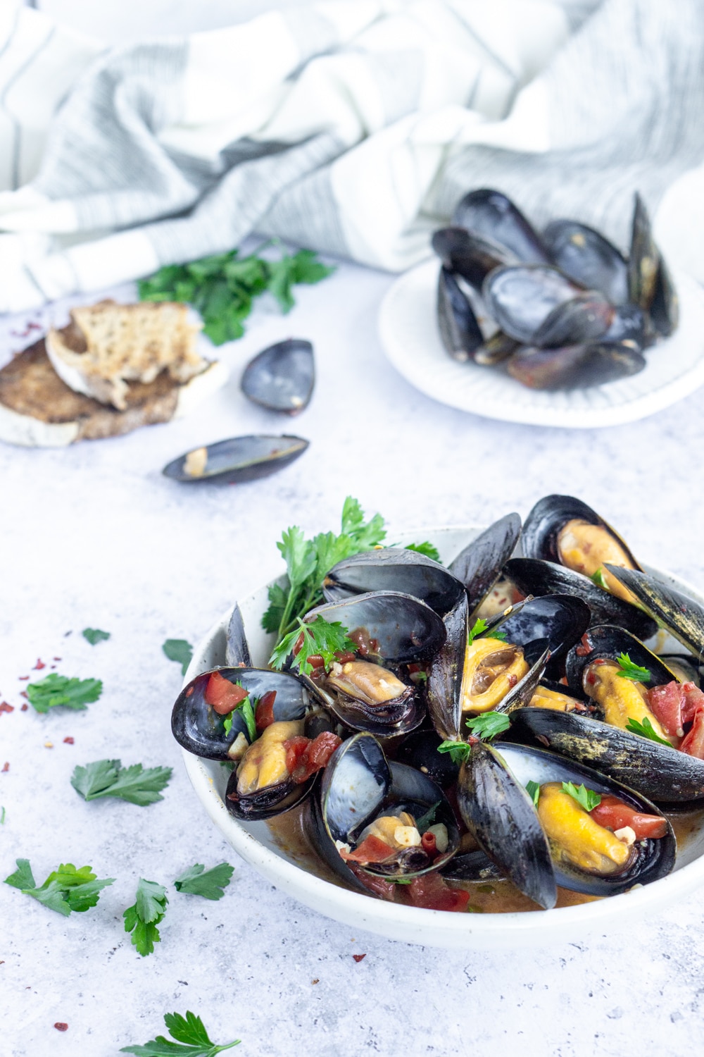 Easy steamed mussels with white wine, garlic and tomato broth. #steamedmussels #mussels #pinacooks #italianfood Side view of a bowl of mussels with mussel shells and bread in the background