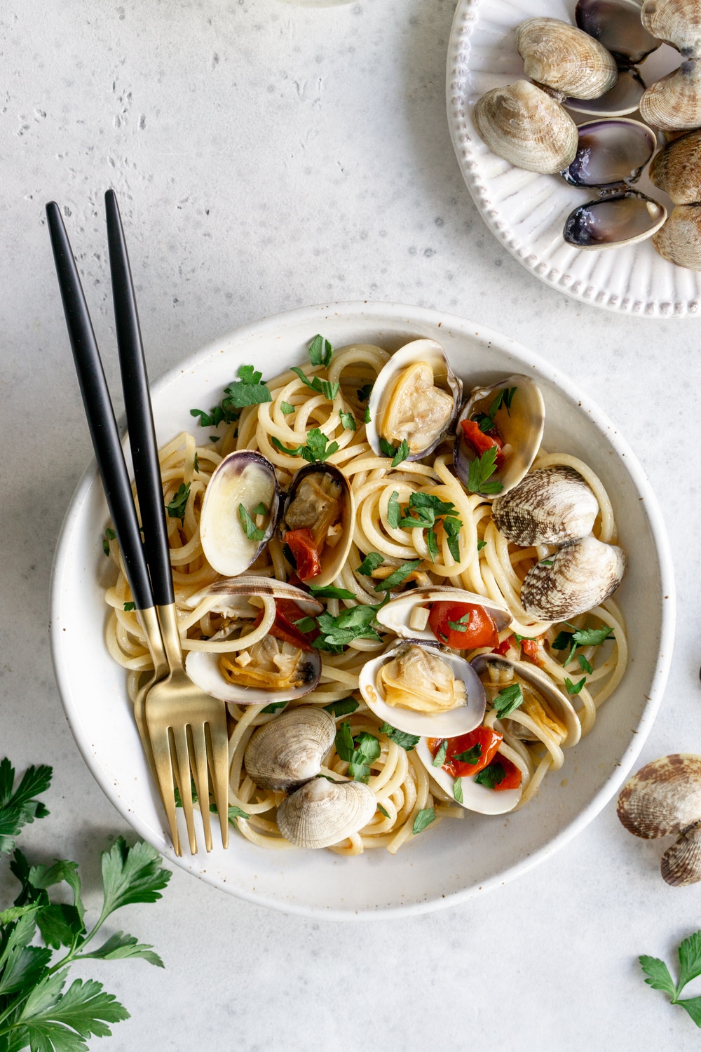 A delicious clam pasta just like they make in Italy! Simple and delicious #pinacooks #clampasta #italianfood Clam pasta in a bowl with two forks, with a buncb of parsley to the left