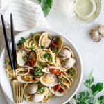 Bowl of clam pasta on a white napkin, surrounded by bunches of parsley