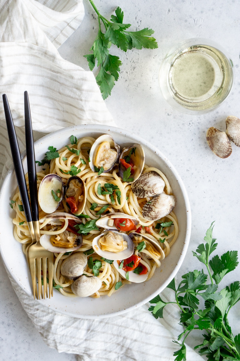 Spaghetti alle Vongole - a recipe reminiscent of Italian seaside towns. #clampasta #italianfood #pinacooks Bowl of clam pasta on a white napkin, surrounded by bunches of parsley
