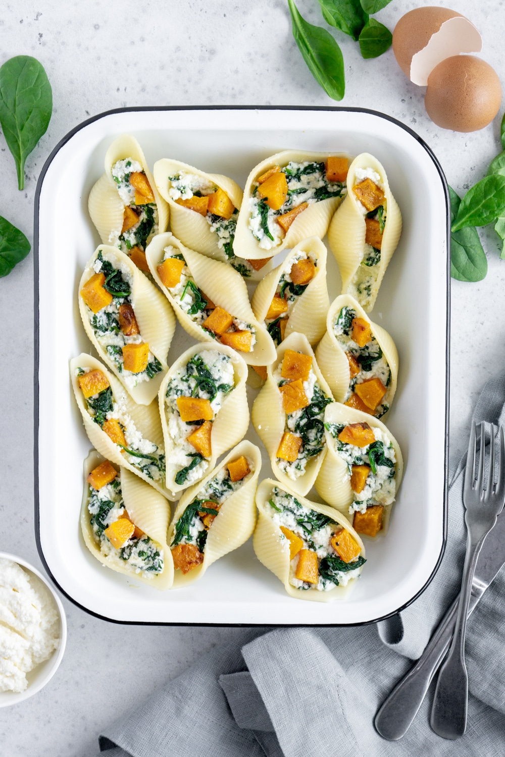 Vegetarian stuffed shells with butternut squash, spinach and ricotta. #stuffedshells #pastashells #pinacooks Stuffed Pasta Shells in a white pan surrounded by spinach and fresh ricotta
