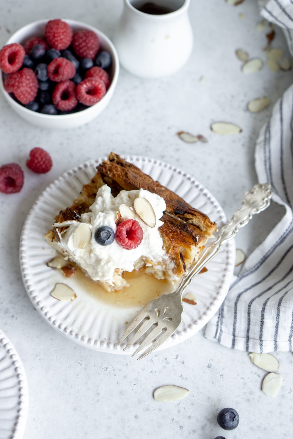 slices of overnight panettone french toast topped with whipped cream in a white dish