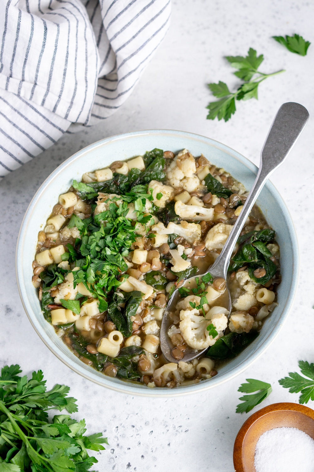 Bowl of lentil soup with a spoon in it surrounded by bits of parsley