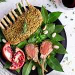 two lamb chops on a plate with a whole rack of lamb on a bed of bay leaves