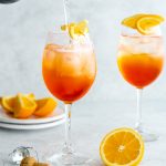2 glasses of aperol spritz with prosecco being poured into one glass