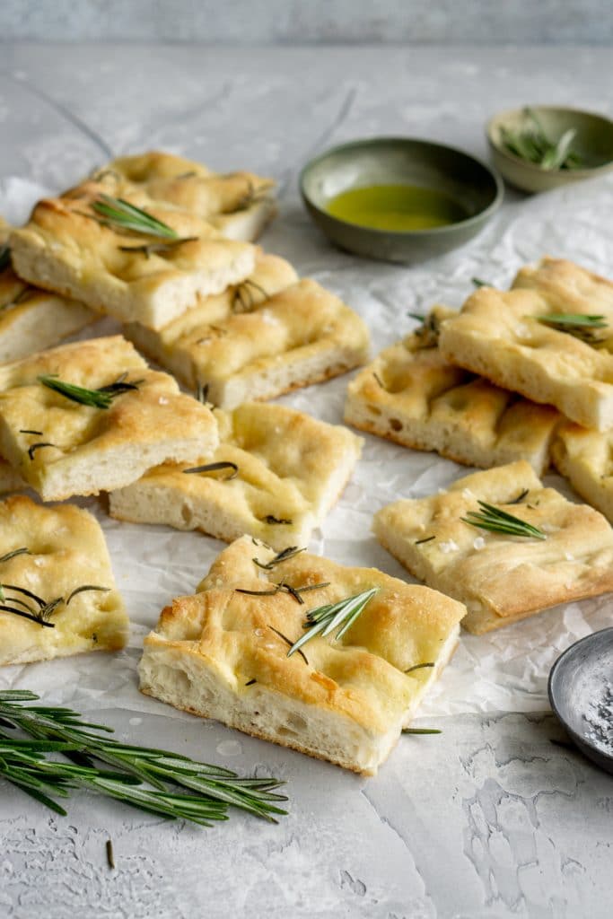 Pies of focaccia pizza on parchment paper with a bowl of olive oil in the background
