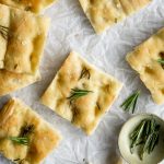 Square pieces of focaccia pizza topped with rosemary on parchment paper