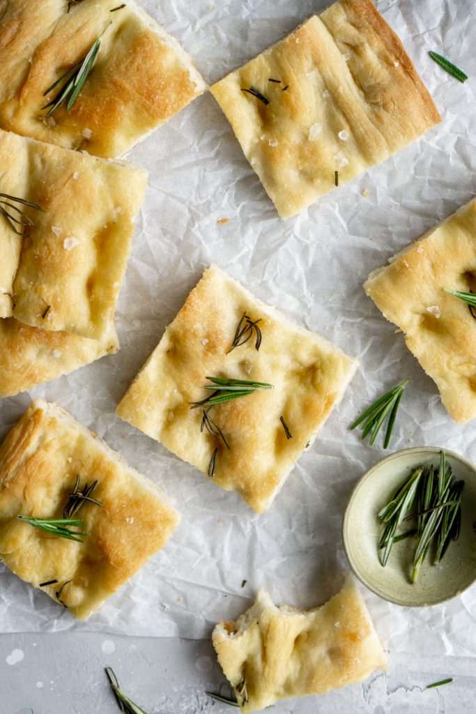 Square pieces of focaccia pizza topped with rosemary on parchment paper
