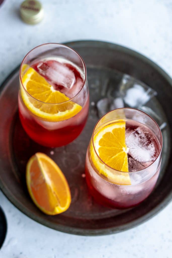 2 glasses of campari and soda garnished with orange slices in a circular steel dish