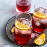 Campari and soda in a tall glass garnished with orange slices and a bottle of campari in the background