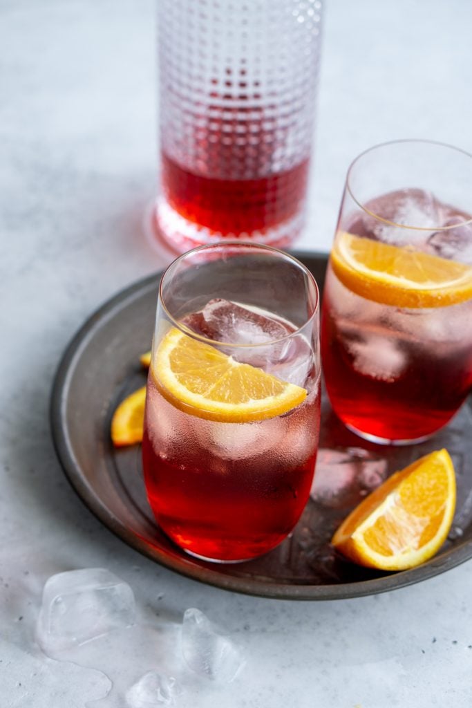 Campari and soda in a tall glass garnished with orange slices and a bottle of campari in the background