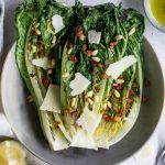 Overhead photo of grilled romaine salad topped with pancetta, pecorino and pine nuts