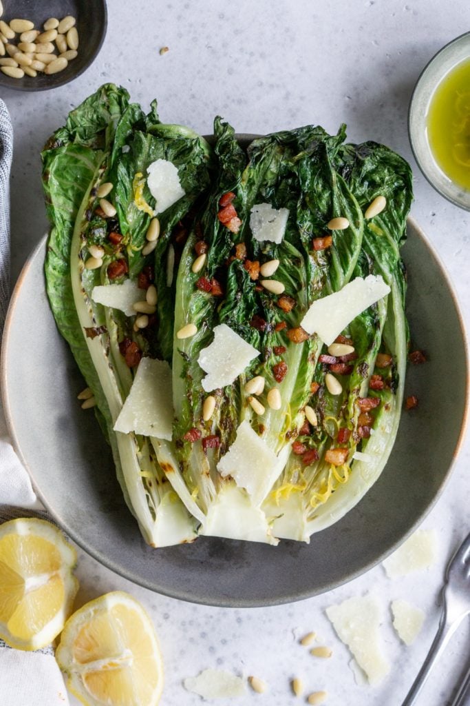 Overhead photo of grilled romaine salad topped with pancetta, pecorino and pine nuts