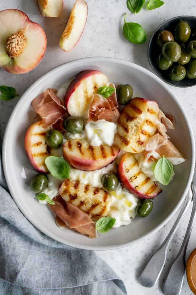 A plate of peach burrata salad with a grey napkin on the side