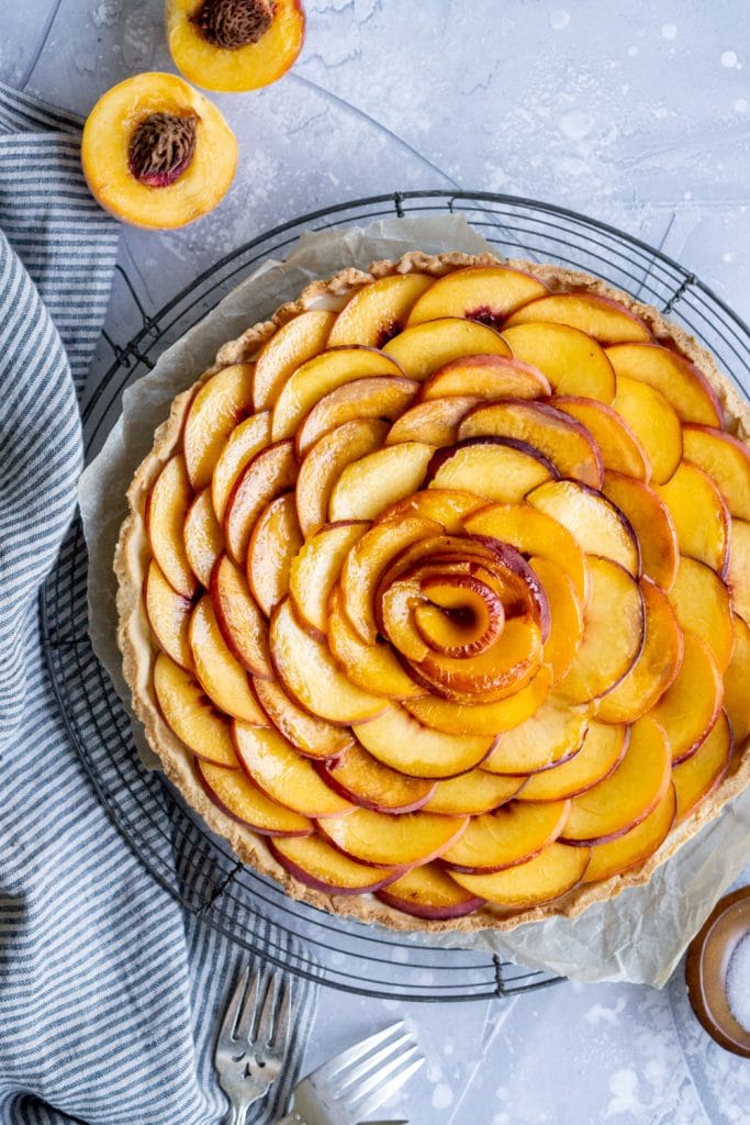 Peach tart on a piece of parchment paper with a halved peach to the side