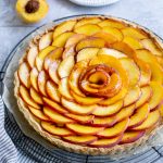 Side view of a peach tart with sliced peaches on a plate in the background
