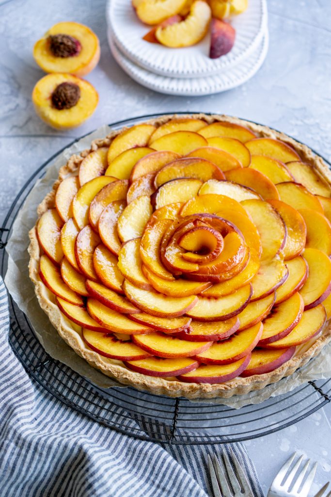 Side view of a peach tart with sliced peaches on a plate in the background